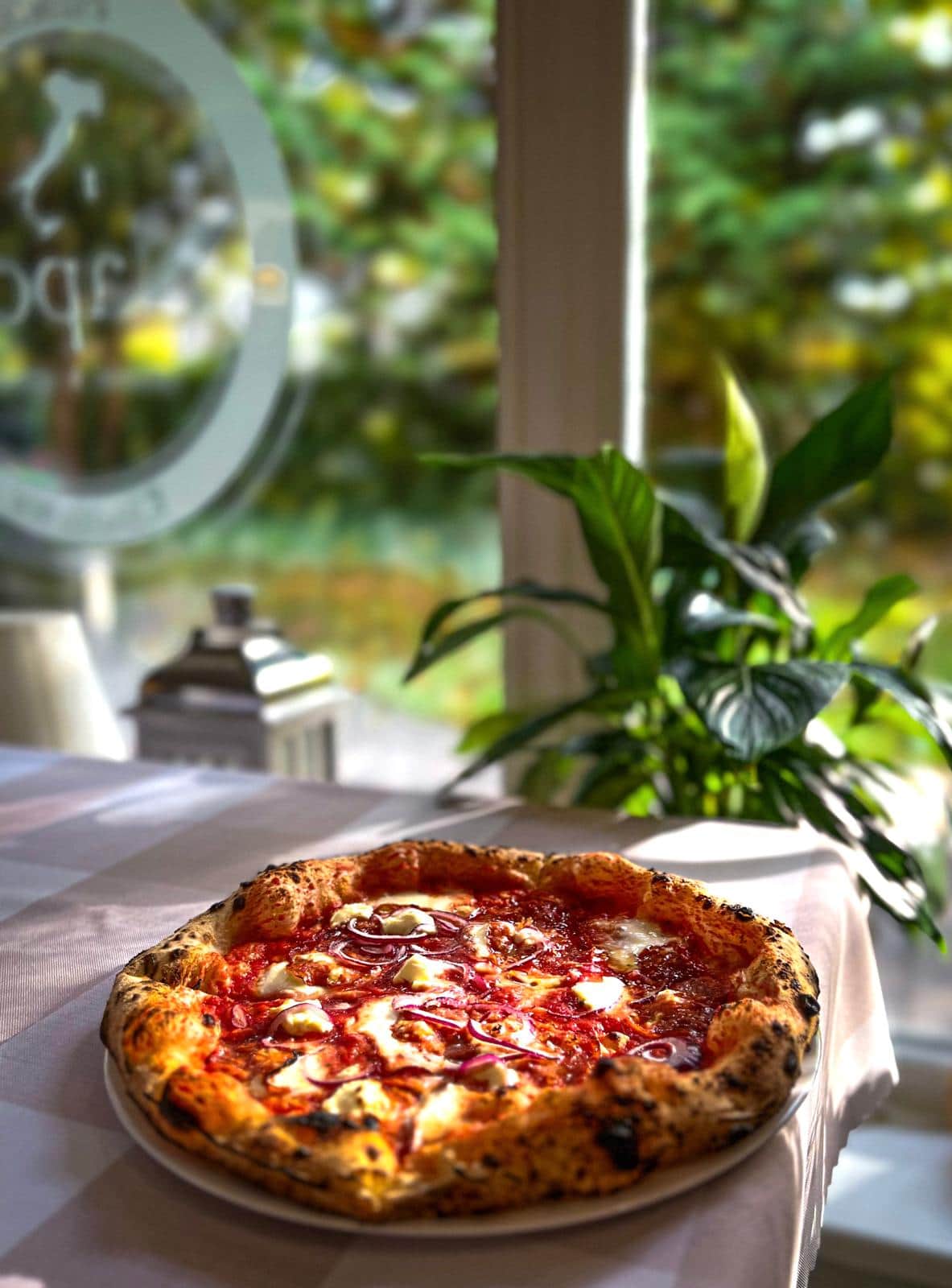 Pizza neapolitańska z mozzarellą i czerwoną cebulą na tle okna z logo Napoli